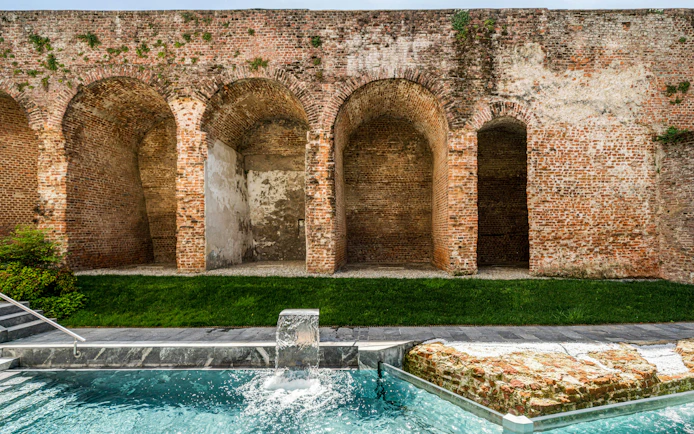 Outdoor pool with waterfall at QC Terme Milan, bordered by historic brick arches.