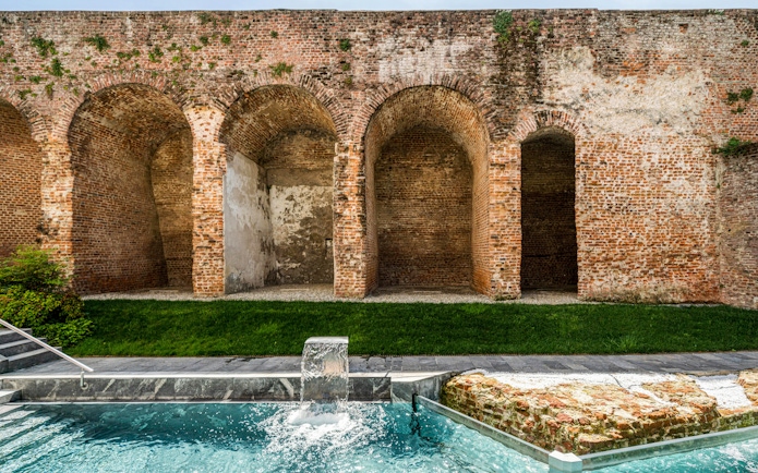 Outdoor pool with waterfall at QC Terme Milan, bordered by historic brick arches.