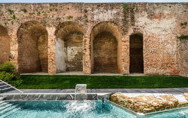 Outdoor pool with waterfall at QC Terme Milan, bordered by historic brick arches.