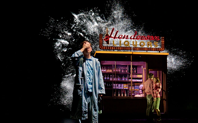 Man in pajamas in front of Henderson Liquors sign, part of Stranger Things: The First Shadow.