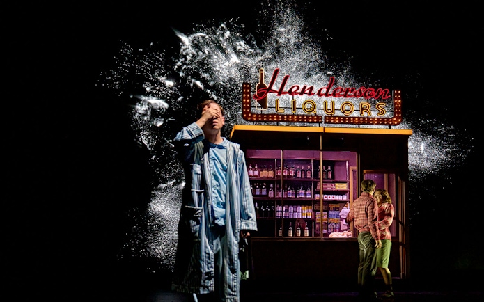 Man in pajamas in front of Henderson Liquors sign, part of Stranger Things: The First Shadow.