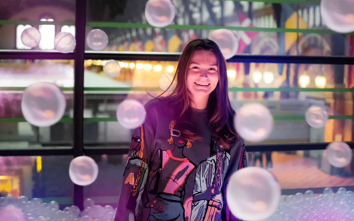 Person smiling inside The TUBE in Copenhagen with colorful lights and bubbles.