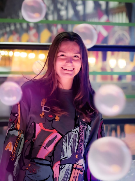 Person smiling inside The TUBE in Copenhagen with colorful lights and bubbles.