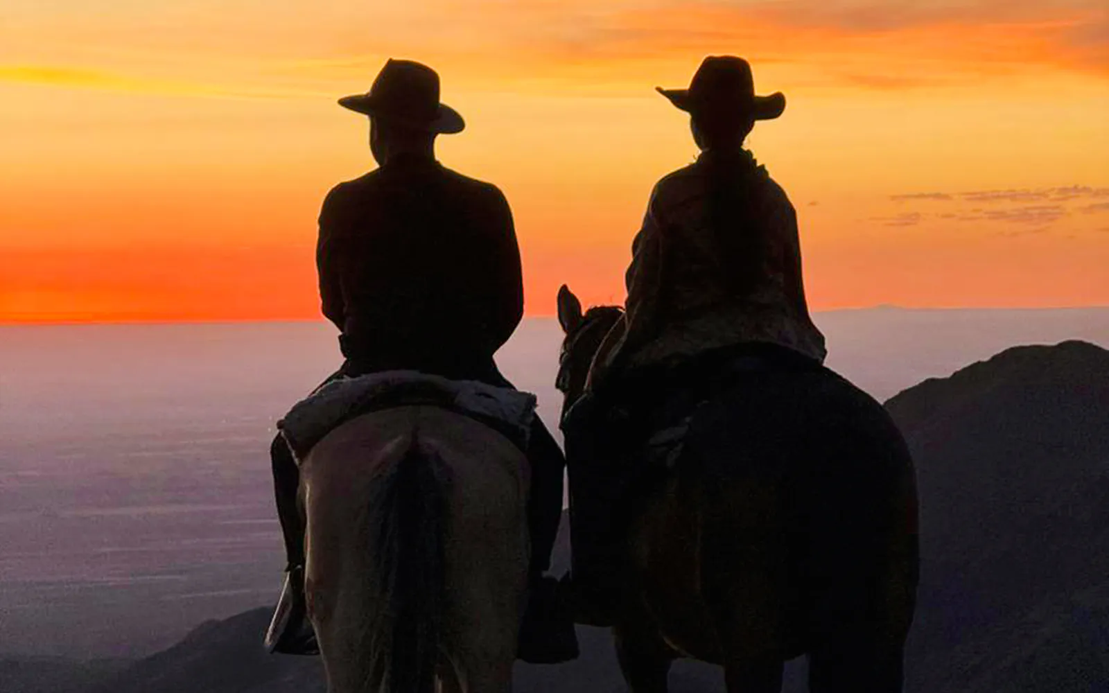 Sunset horse riding in Lunlunta near Mendoza with two riders silhouetted against the sky.