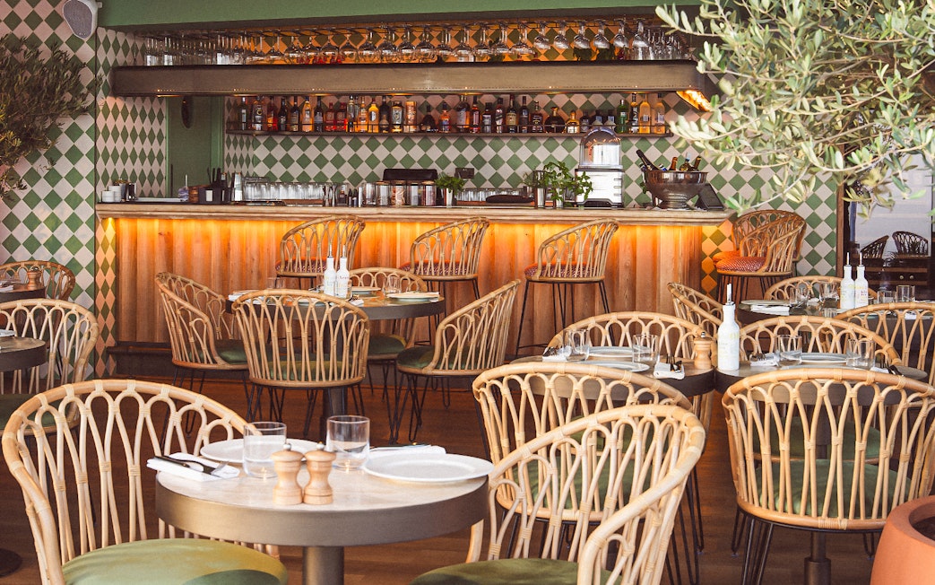 Rattan chairs and set tables in a stylish restaurant with a bar, offering a scenic lunch view.