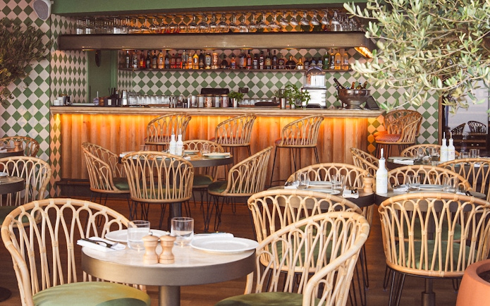 Rattan chairs and set tables in a stylish restaurant with a bar, offering a scenic lunch view.