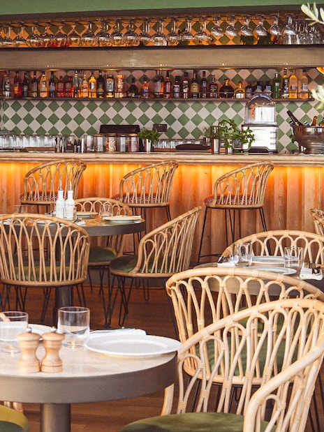 Rattan chairs and set tables in a stylish restaurant with a bar, offering a scenic lunch view.