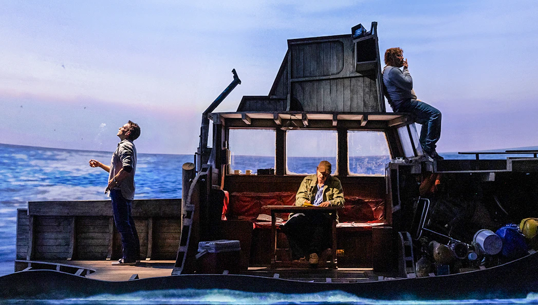 Actors on a boat set during "The Shark is Broken" play, ocean backdrop.