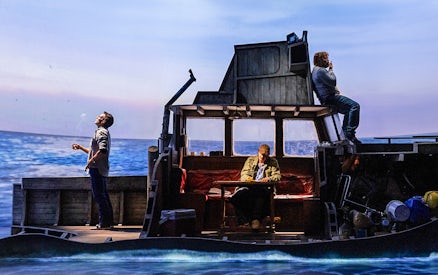 Actors on a boat set during "The Shark is Broken" play, ocean backdrop.