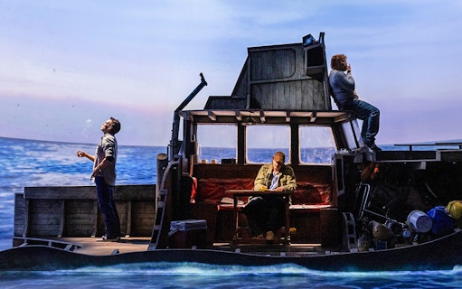 Actors on a boat set during "The Shark is Broken" play, ocean backdrop.