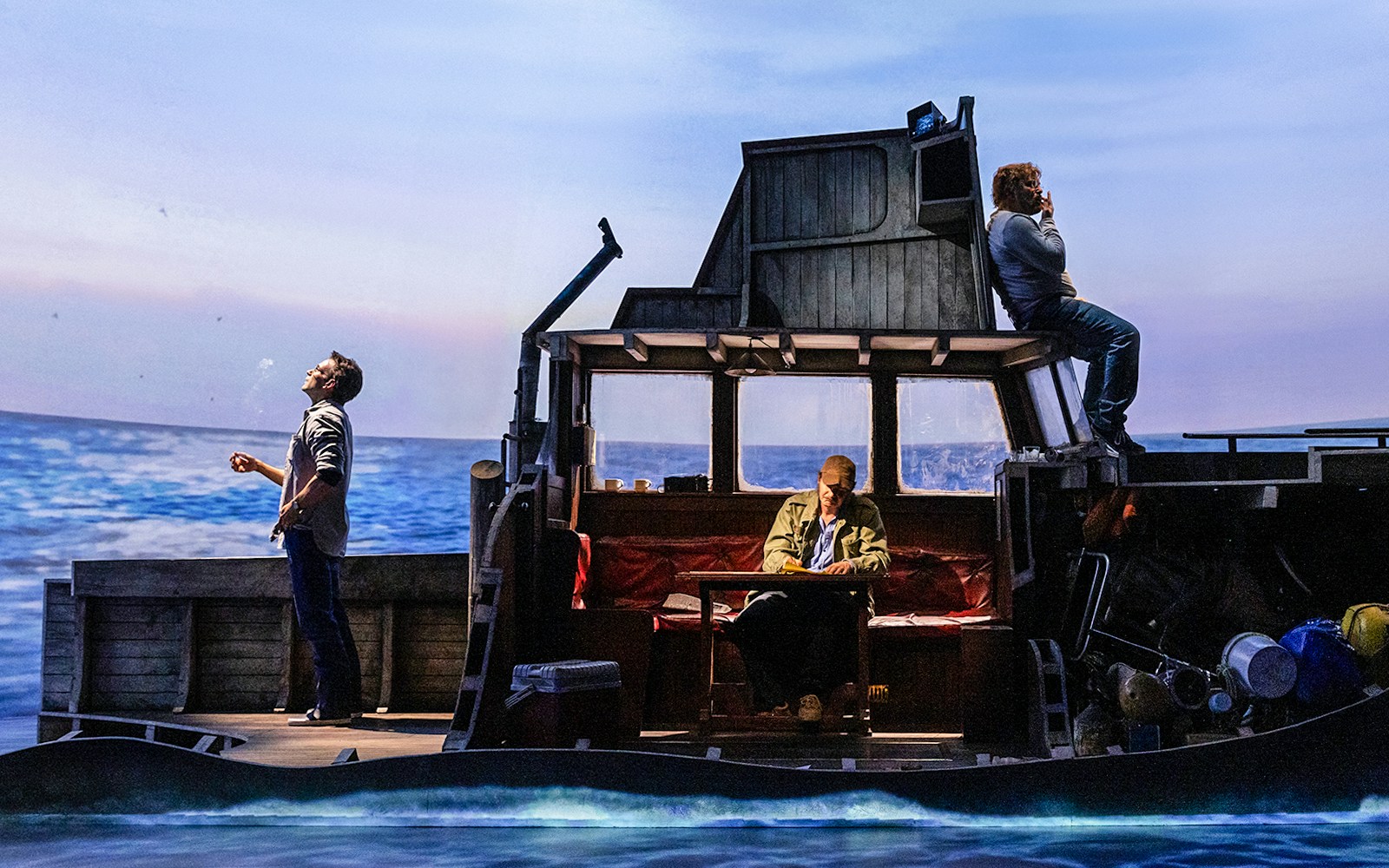 Actors on a boat set during "The Shark is Broken" play, ocean backdrop.