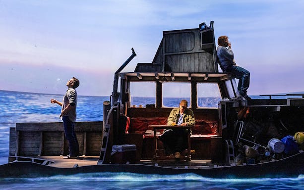 Actors on a boat set during "The Shark is Broken" play, ocean backdrop.