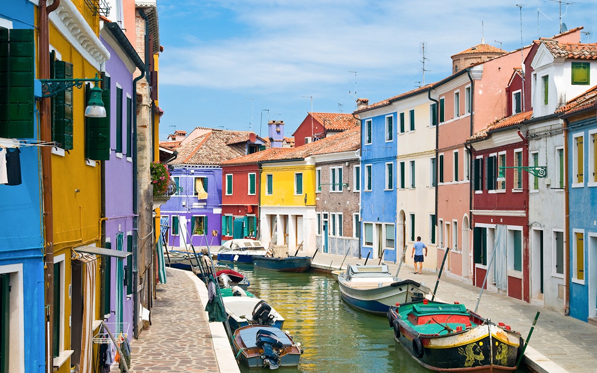 Colorful buildings along Burano canals with boats docked in Venice, Italy.