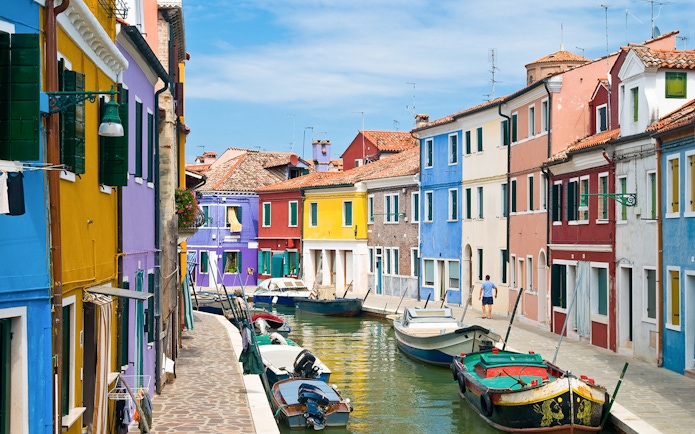 Colorful buildings along Burano canals with boats docked in Venice, Italy.