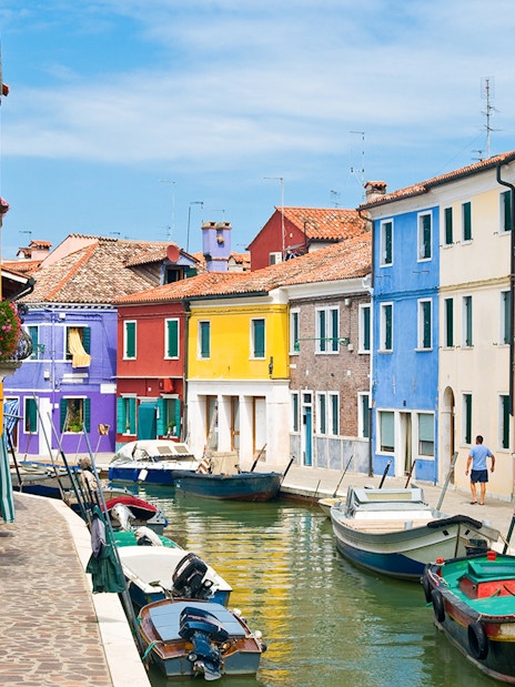 Colorful buildings along Burano canals with boats docked in Venice, Italy.