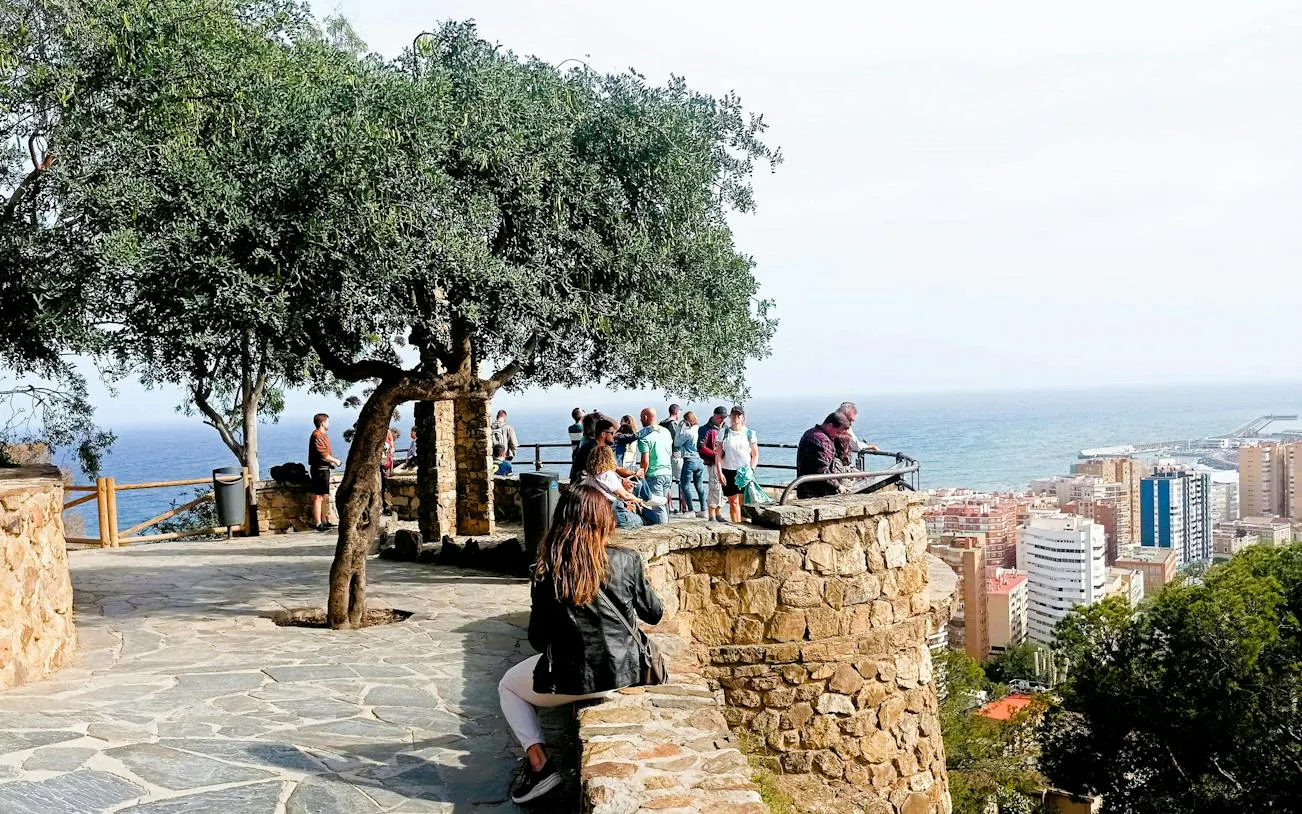 Visitors enjoying a scenic view of Malaga city and coastline from a stone terrace.
