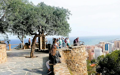 Visitors enjoying a scenic view of Malaga city and coastline from a stone terrace.