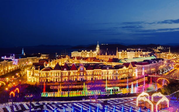 Huis Ten Bosch illuminated at night with colorful lights, seen on a 1-day bus tour from Fukuoka Airport.