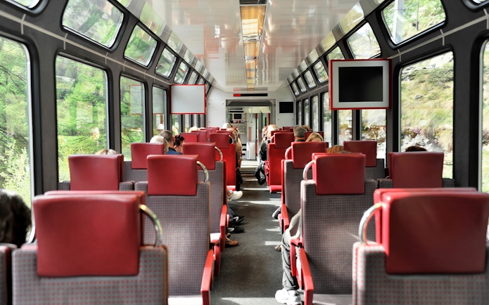 Passengers seated inside Zermatt shuttle train with Swiss Alps views through windows.