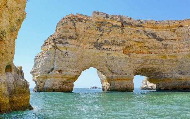 Boat approaching Benagil Caves' natural arches in Algarve, Portugal.
