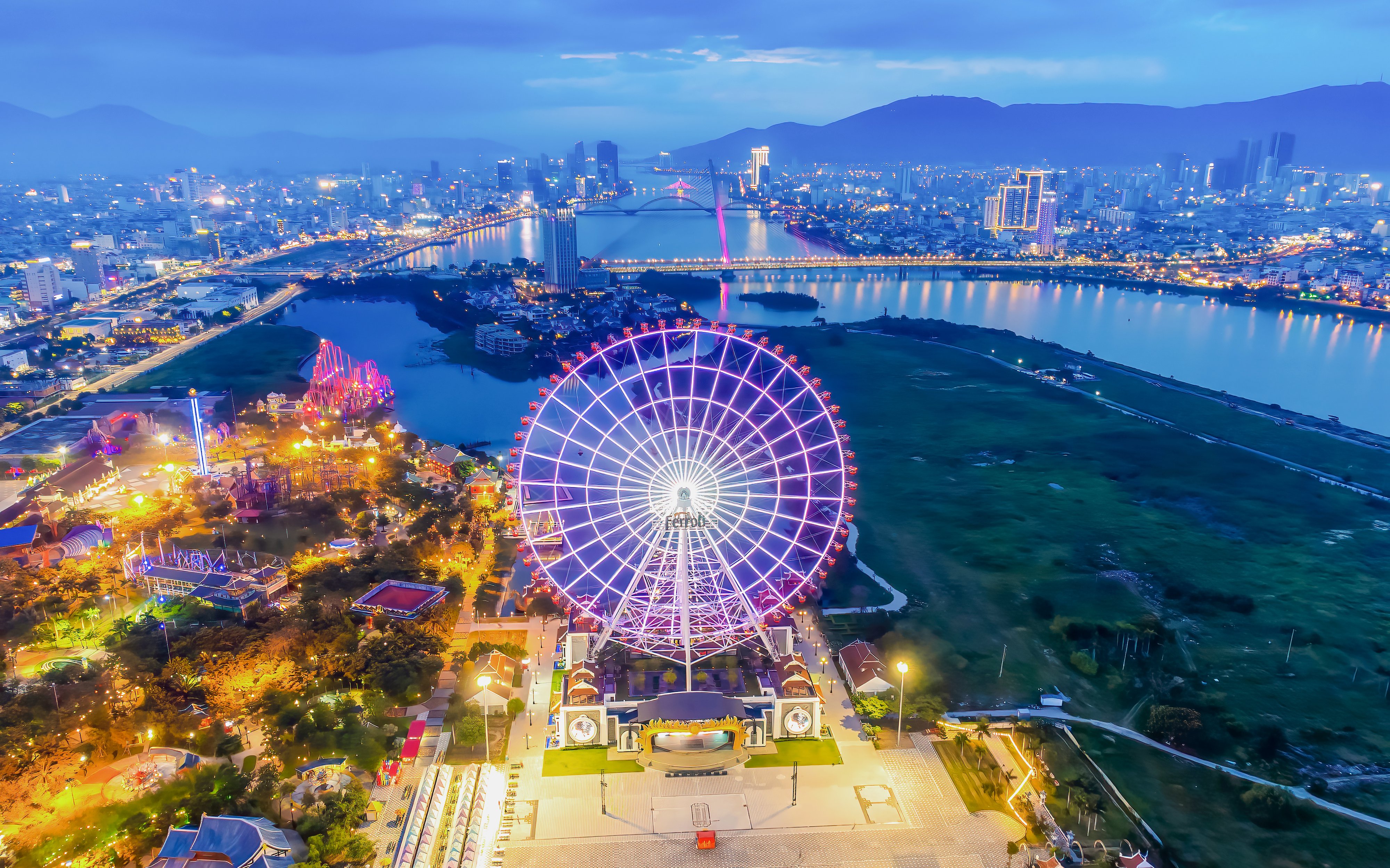 Ferris wheel illuminated at night in downtown Da Nang, Vietnam with cityscape and river.