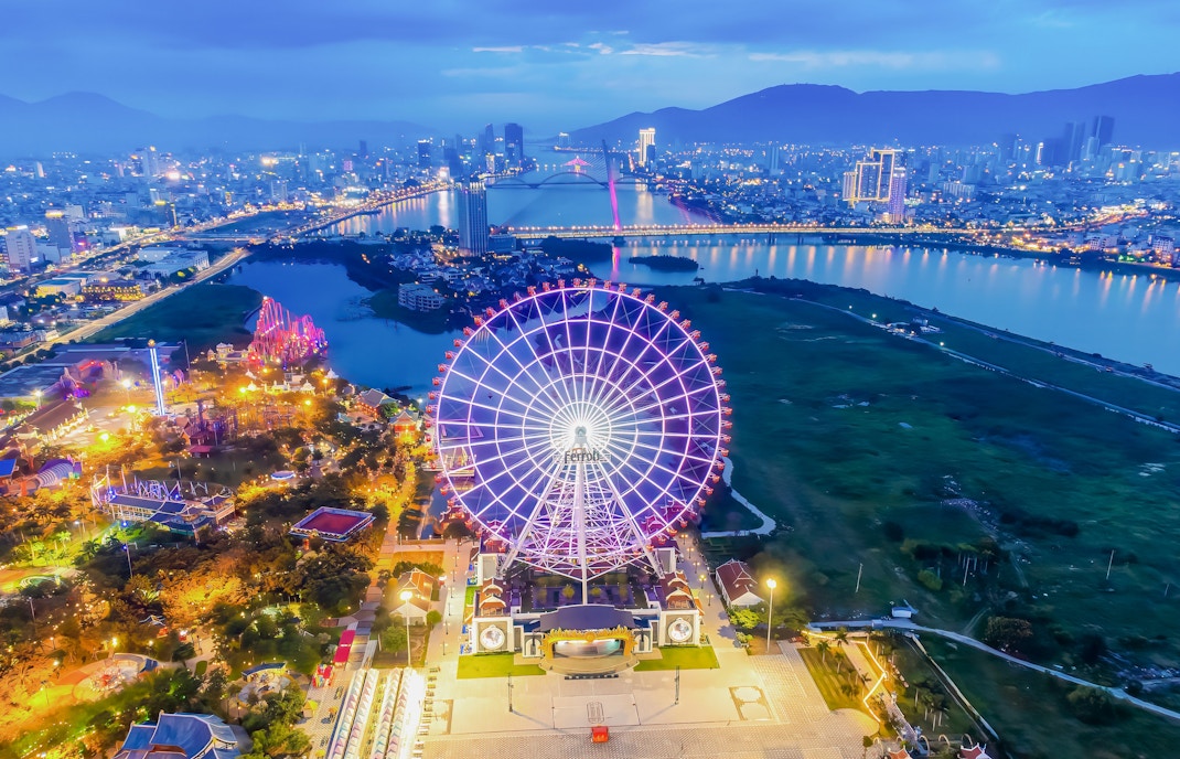 Ferris wheel illuminated at night in downtown Da Nang, Vietnam with cityscape and river.