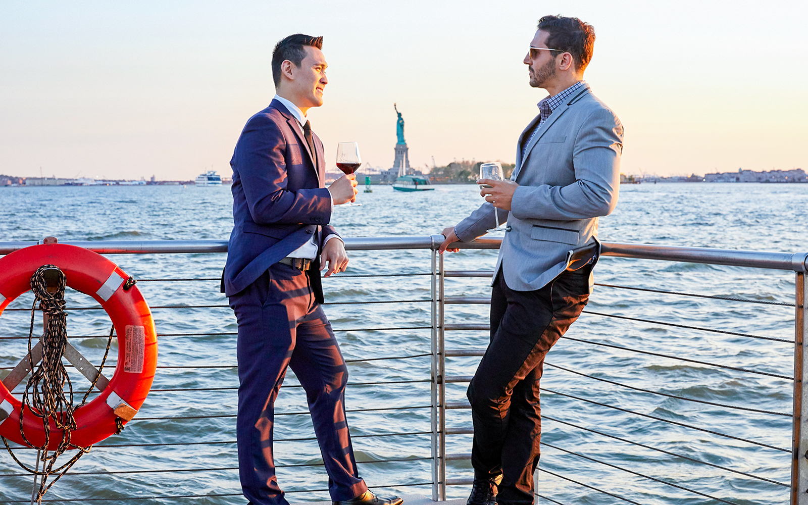 Two people enjoying drinks on a New York dinner cruise with the Statue of Liberty in the background.