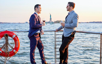 Two people enjoying drinks on a New York dinner cruise with the Statue of Liberty in the background.