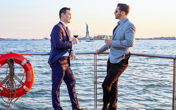 Two people enjoying drinks on a New York dinner cruise with the Statue of Liberty in the background.