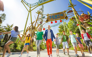 Visitors exploring Exotic World theme park entrance with roller coaster overhead.