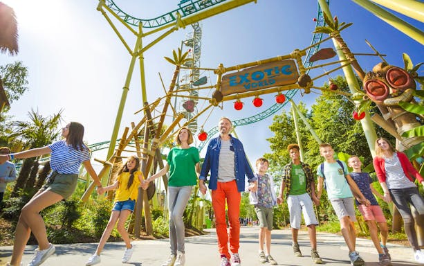 Visitors exploring Exotic World theme park entrance with roller coaster overhead.