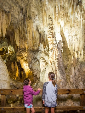 Children observing stalactites and stalagmites inside Aranui Cave, New Zealand.