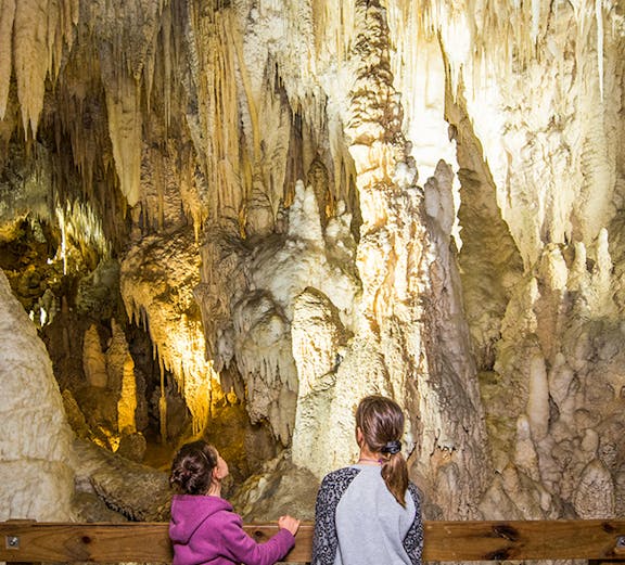 Children observing stalactites and stalagmites inside Aranui Cave, New Zealand.