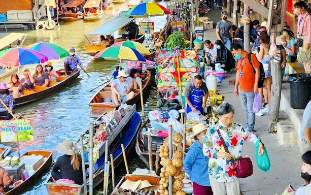 Tourists navigating boats at Damnoen Saduak Floating Market, Thailand, with colorful stalls.