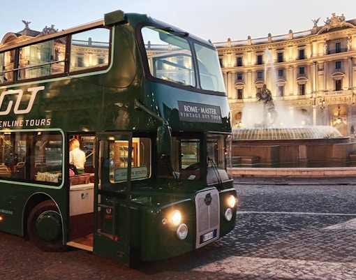 Vintage open-top double-decker bus touring Rome at night with city lights.
