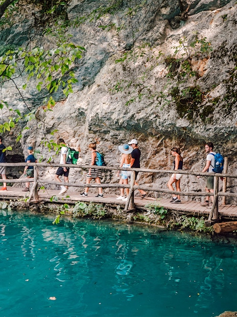 Tour group walking on a wooden path by turquoise water at Plitvice Lakes National Park.