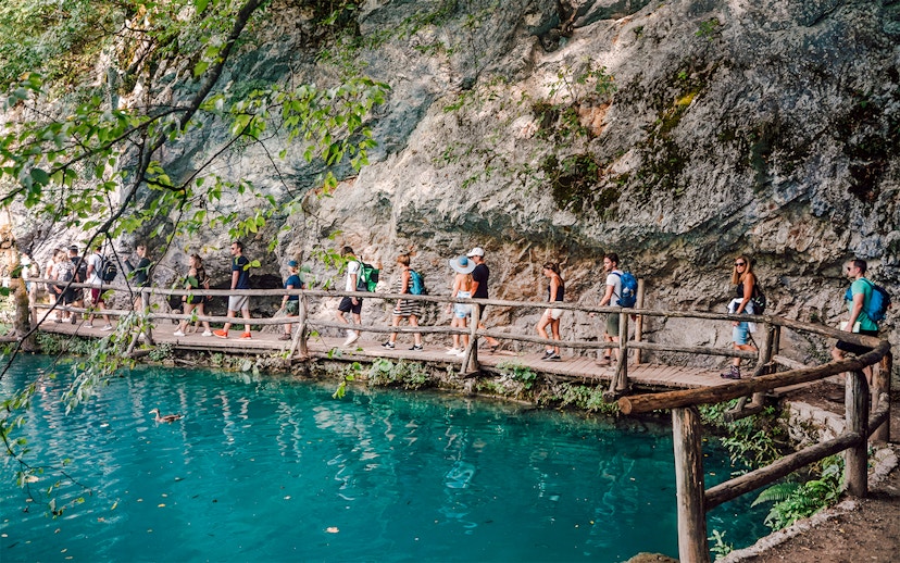 Tour group walking on a wooden path by turquoise water at Plitvice Lakes National Park.