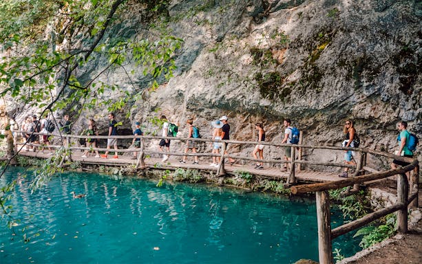 Tour group walking on a wooden path by turquoise water at Plitvice Lakes National Park.
