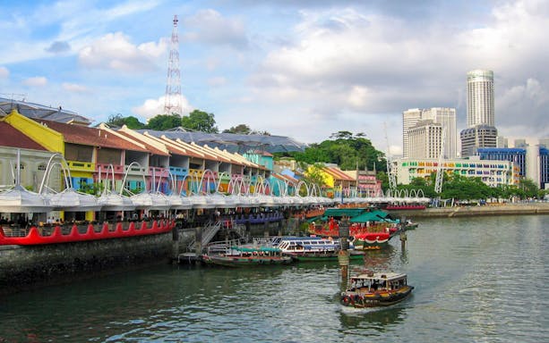 Colorful buildings along Singapore River with boats and city skyline in the background.