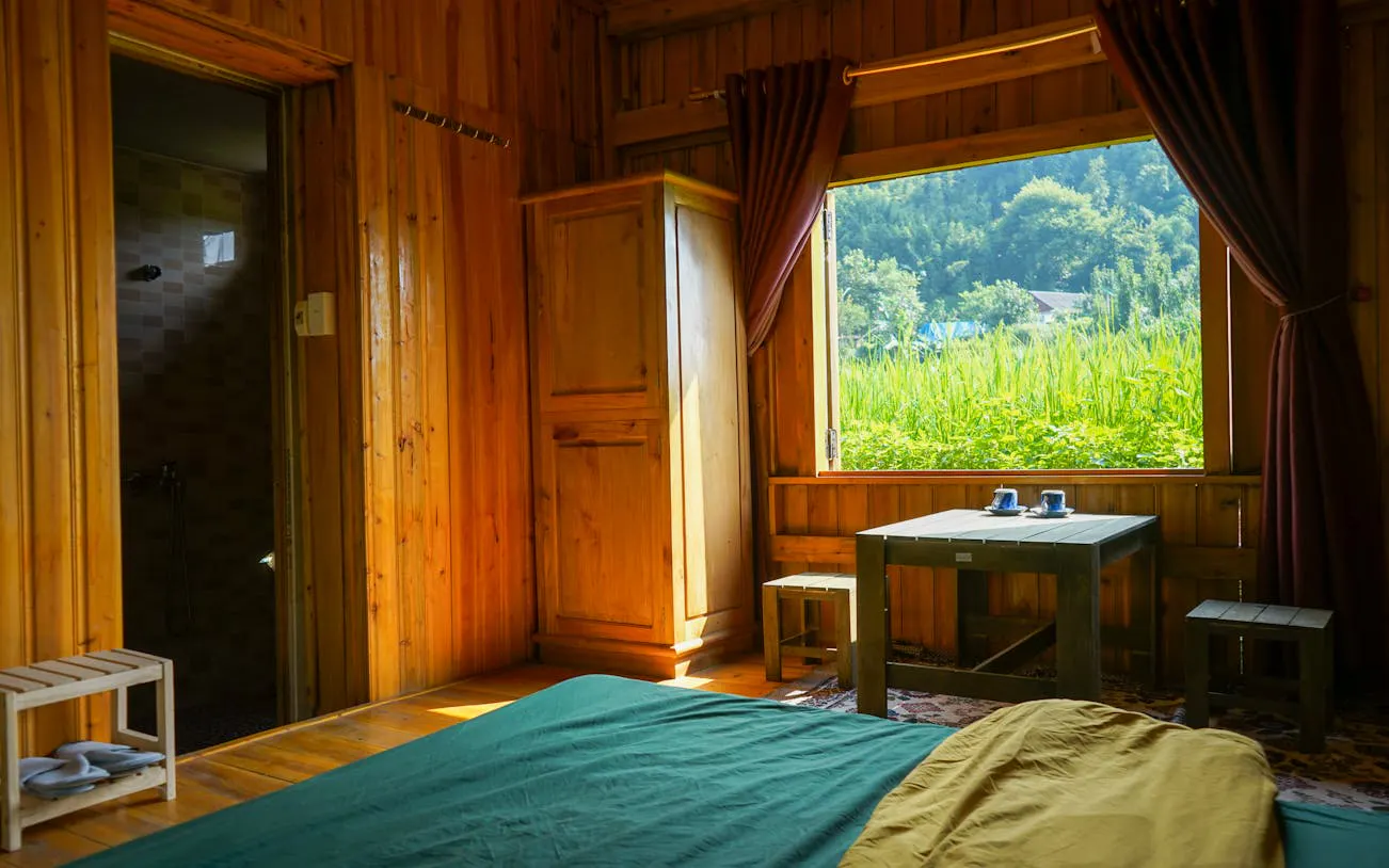 Interior of a Giay homestay room with wooden walls, table, and view of lush greenery in Ta Van.