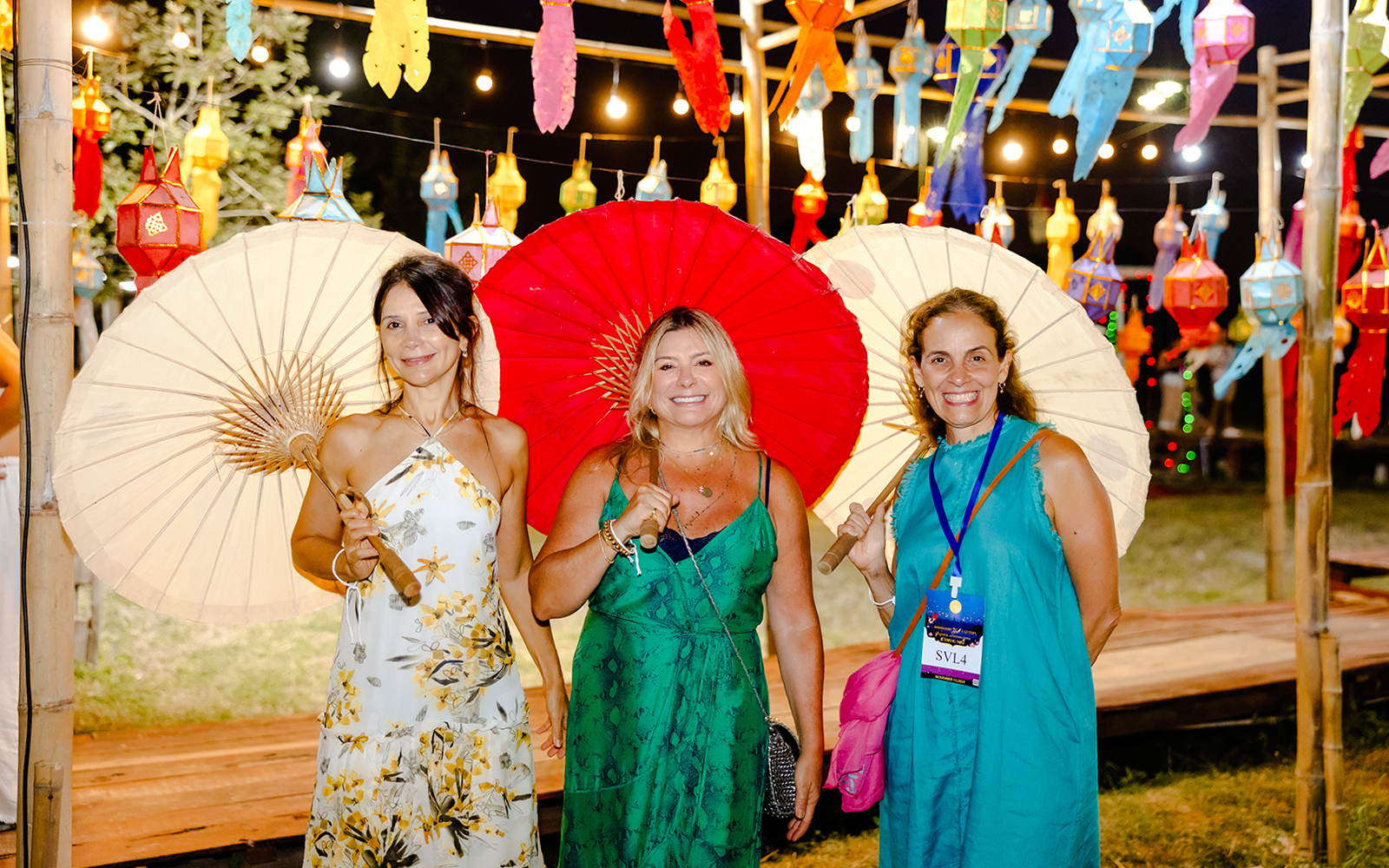 Three women with paper umbrellas under colorful lanterns at Yi Peng and Loy Krathong Festival, Chiang Mai 2025.