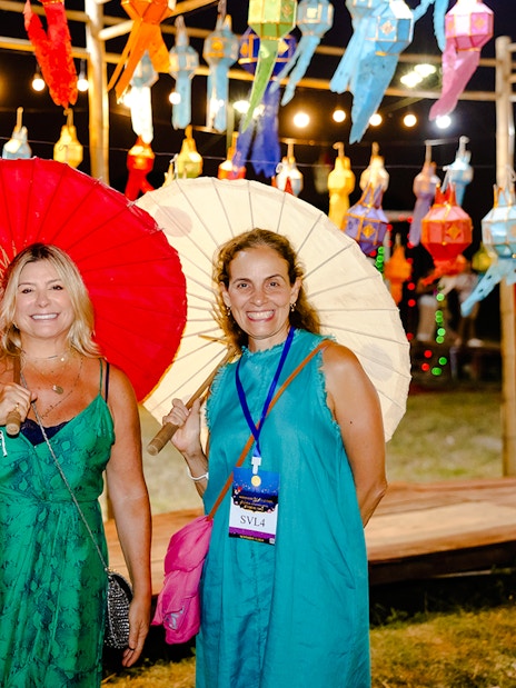 Three women with paper umbrellas under colorful lanterns at Yi Peng and Loy Krathong Festival, Chiang Mai 2025.