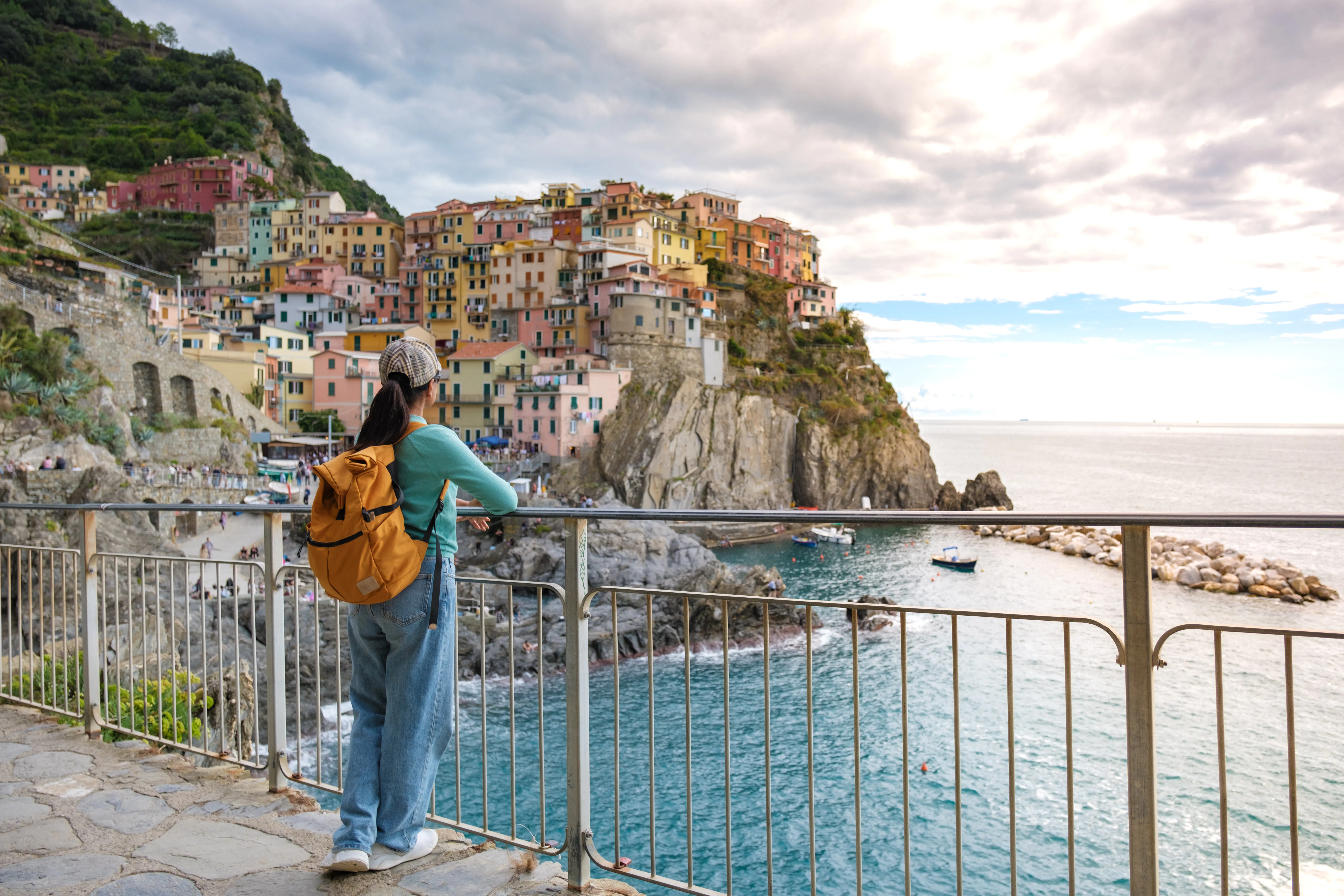 Traveler overlooking colorful buildings and coastline in Manarola, Cinque Terre during evening.
