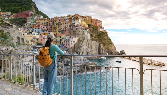 Traveler overlooking colorful buildings and coastline in Manarola, Cinque Terre during evening.