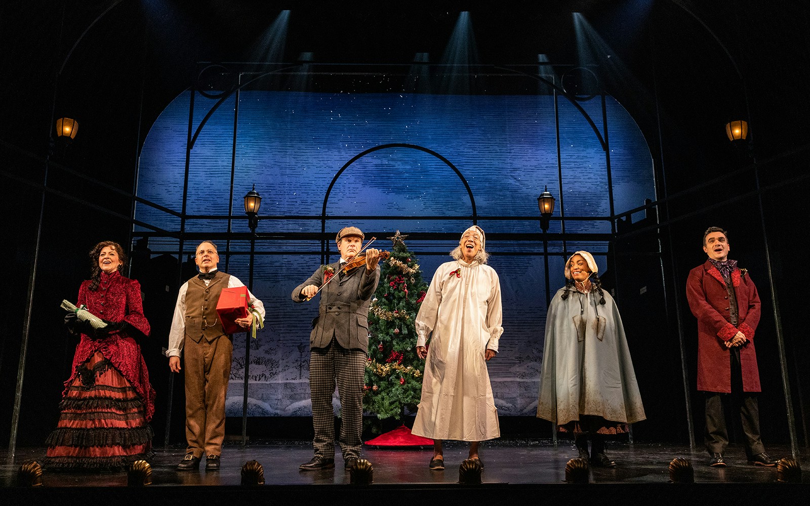 Actors on stage performing "A Sherlock Carol" with a Christmas tree backdrop.