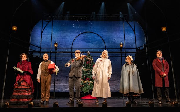 Actors on stage performing "A Sherlock Carol" with a Christmas tree backdrop.