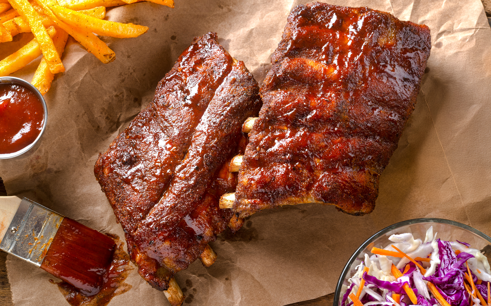 Grilled baby back pork ribs on a wooden platter with dipping sauce.