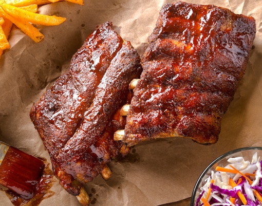 Grilled baby back pork ribs on a wooden platter with dipping sauce.