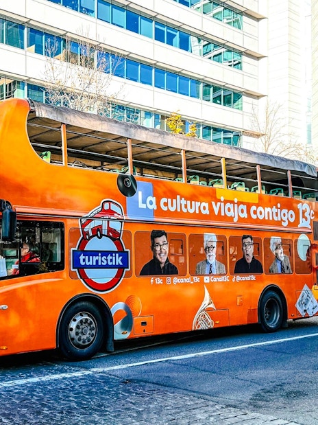 Orange double-decker bus for Santiago Hop on Hop off tour on city street.