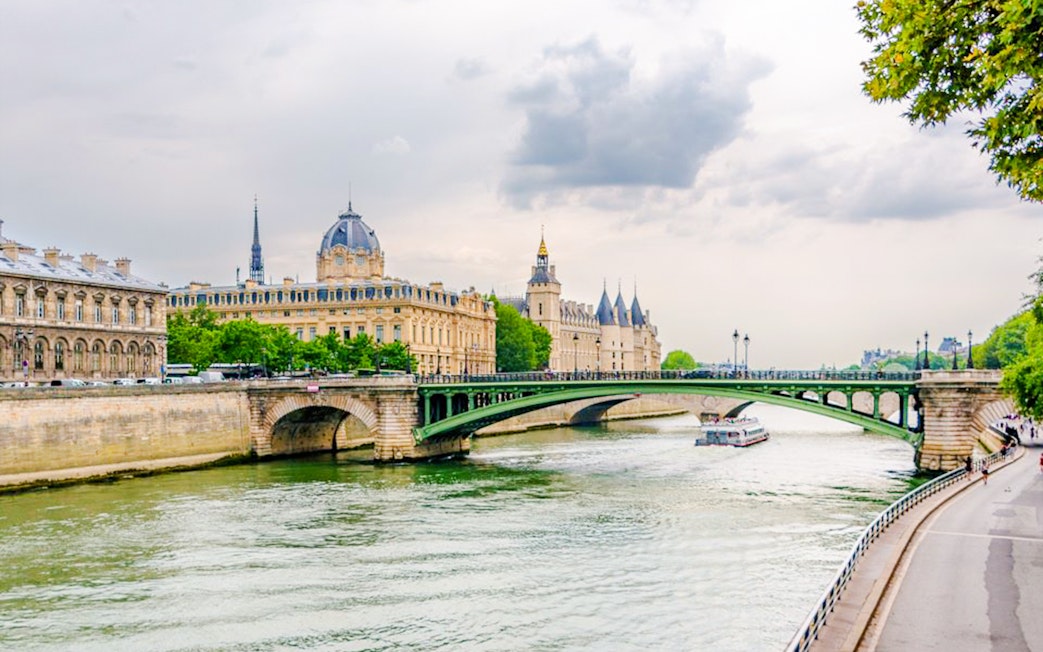 Seine River cruise boat passing under a bridge with historic Parisian architecture in the background.
